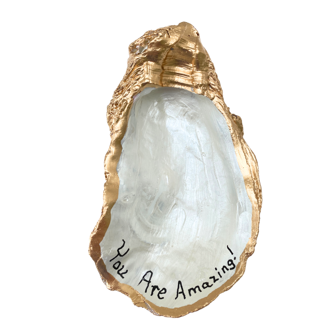 A handpainted large oyster shell art with the message 'You Are Amazing' written in black ink, with gold leaf detailing on the edges.