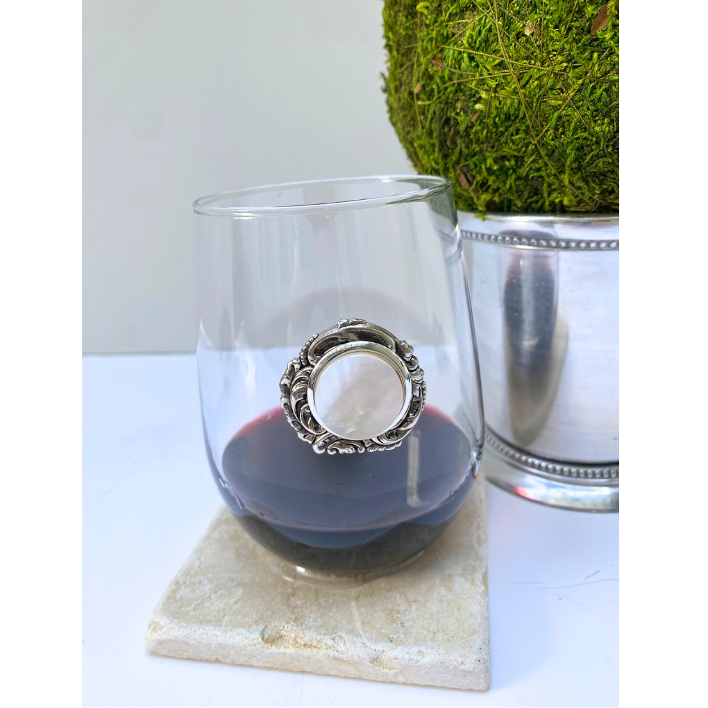 Clear glass with a Mother-of-pearl cabochon decorative ring inside, placed on a marble coaster with a plant in the background.