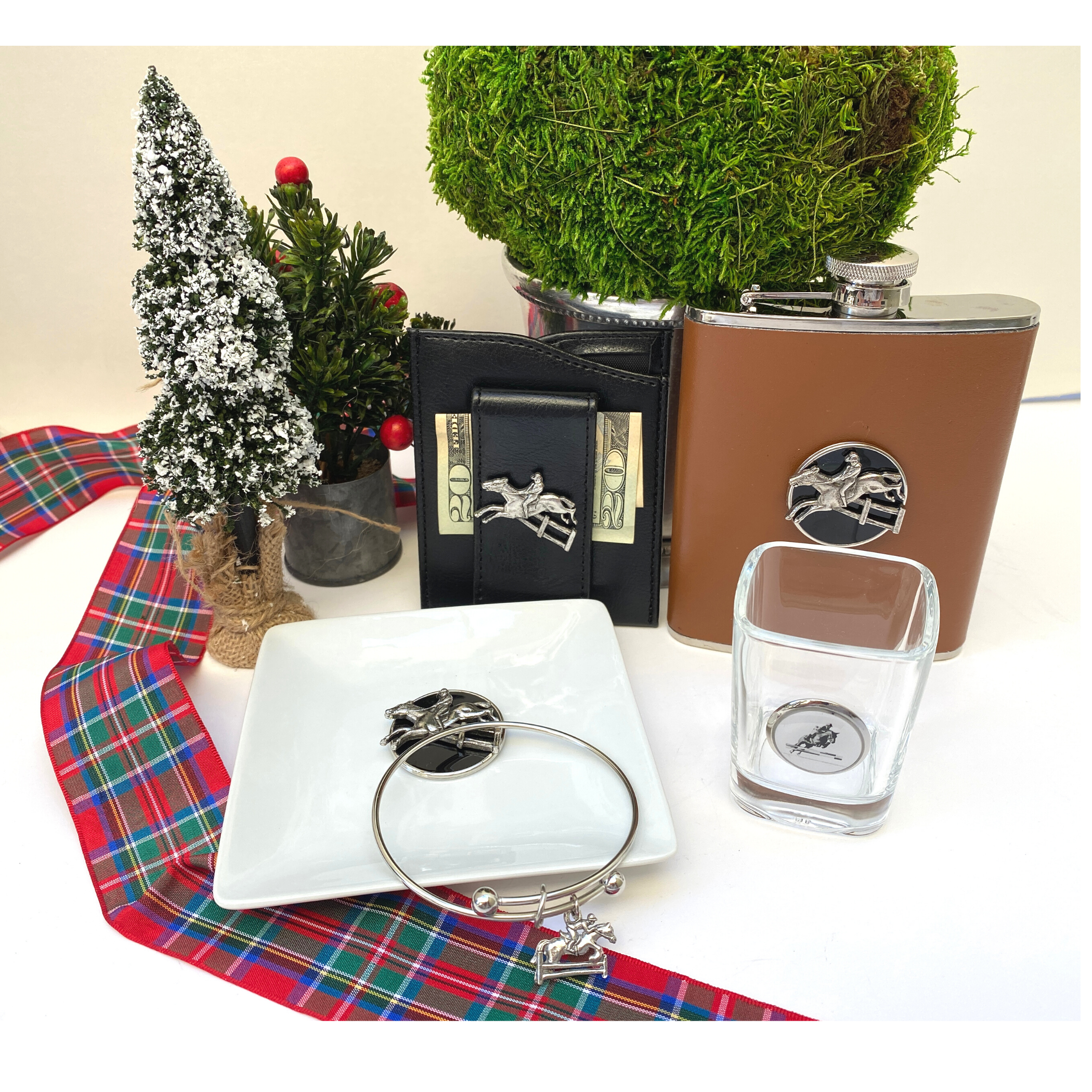 A gift box set containing a leather flask, a bracelet, a trinket tray, a shot glass, and a faux leather money clip wallet, all embellished with a silver hunter jumper medallion.