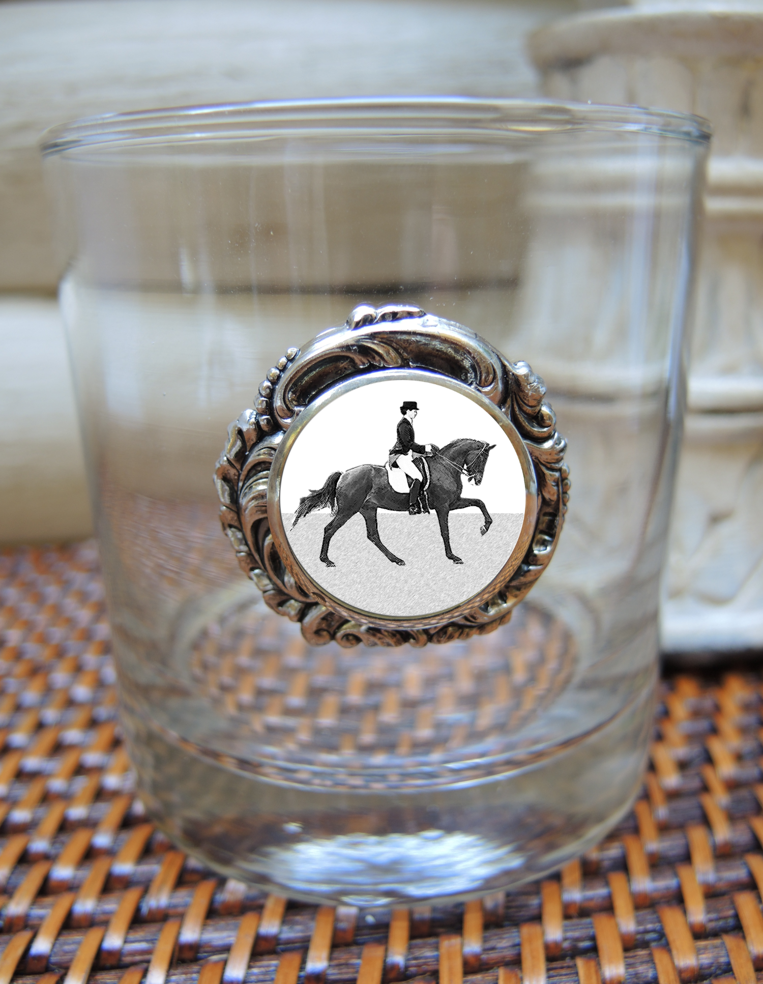 A bourbon glass with a silver dressage medallion featuring a black and white image of a person riding a horse.