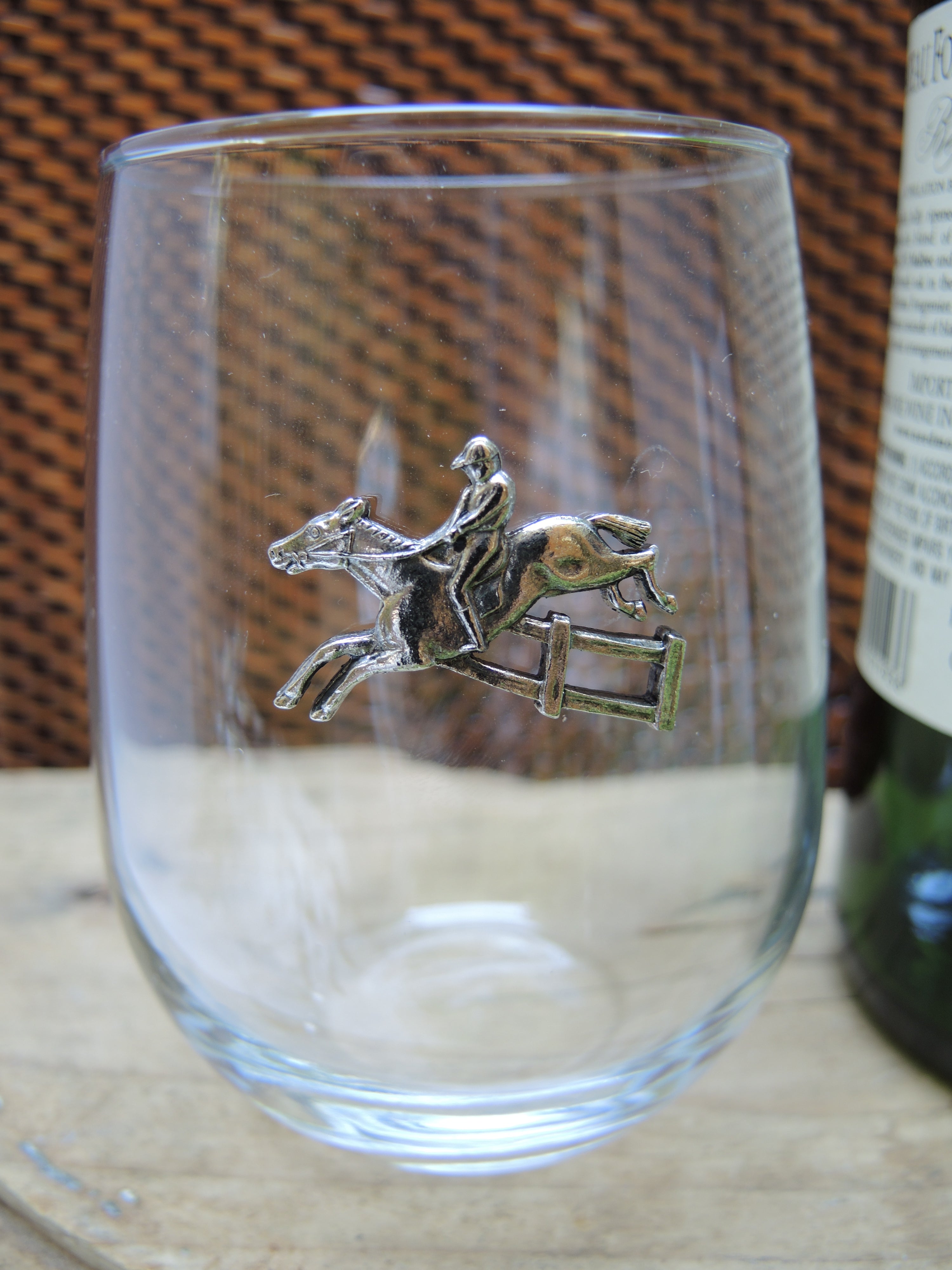 A clear stemless wine glass with a silver medallion of a horse and rider mounted on the side.