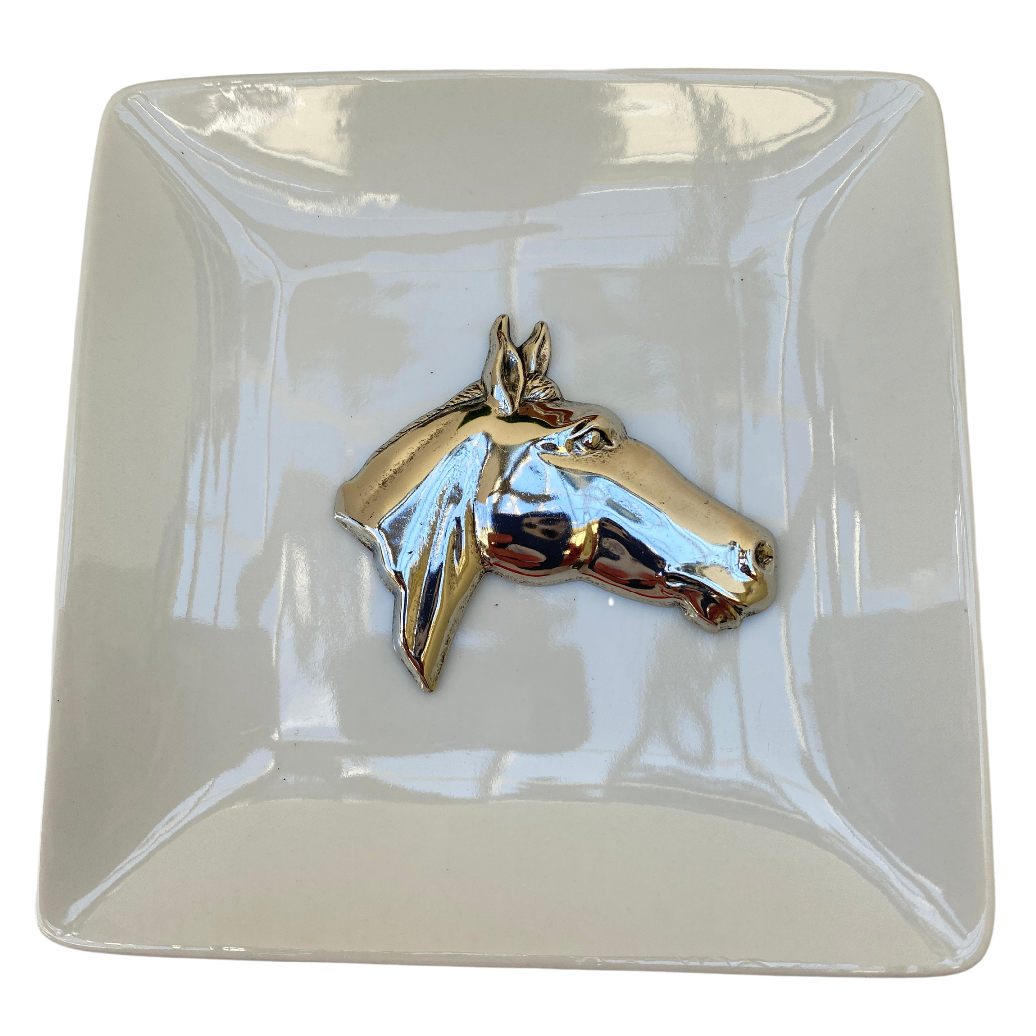 A square white trinket tray with a metallic silver horse head medallion placed on it.