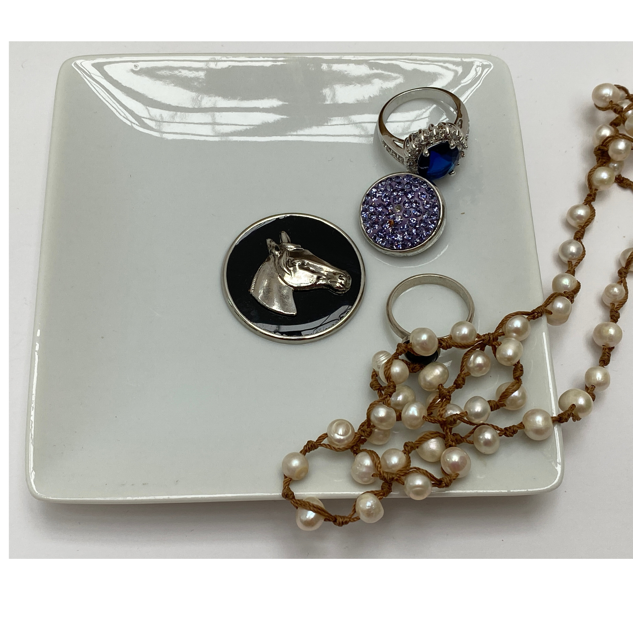 A silver trinket tray with a black enamel horse head medallion and various trinkets placed on its surface.