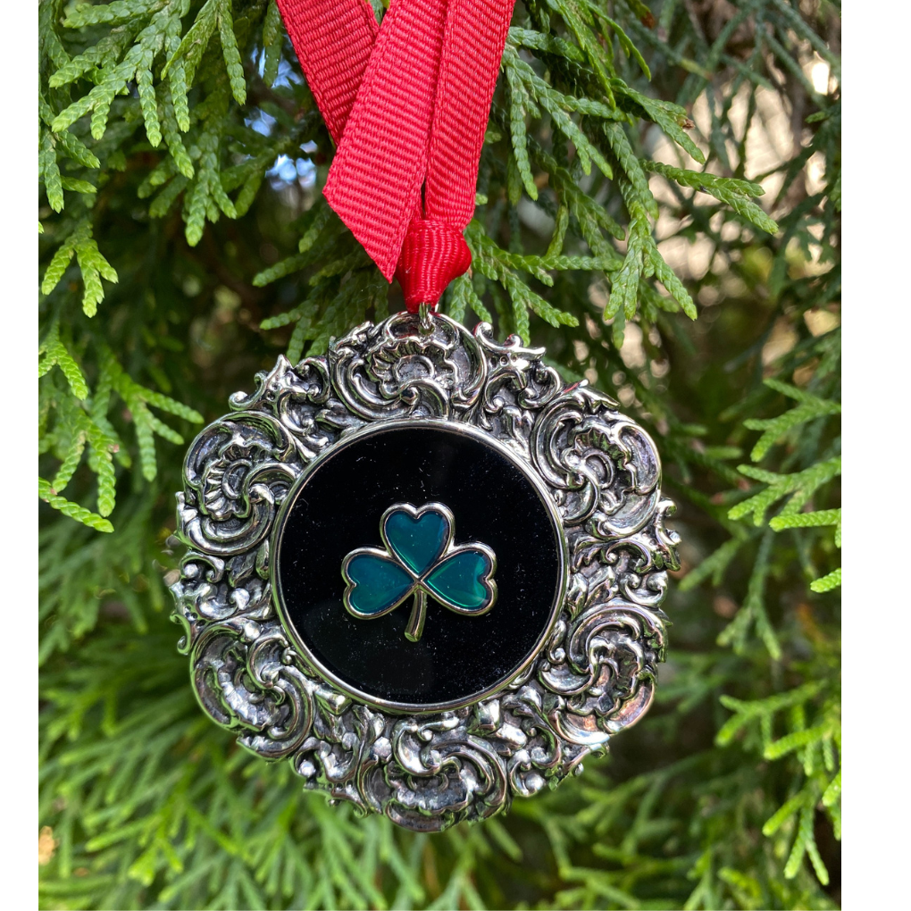 Decorative ornament with shamrock design on a red ribbon against a green tree background