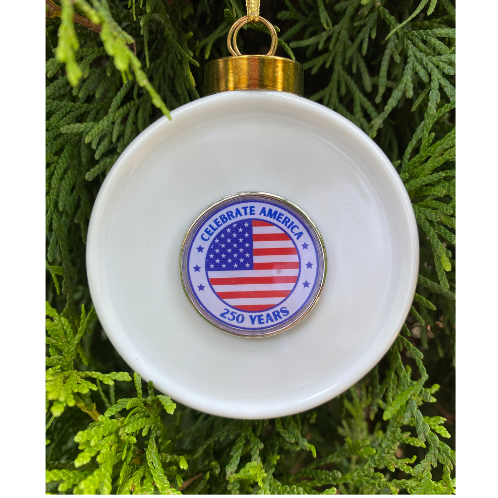 White ornament with American flag design and 'Celebrate America 250 Years' text, hanging on a tree.