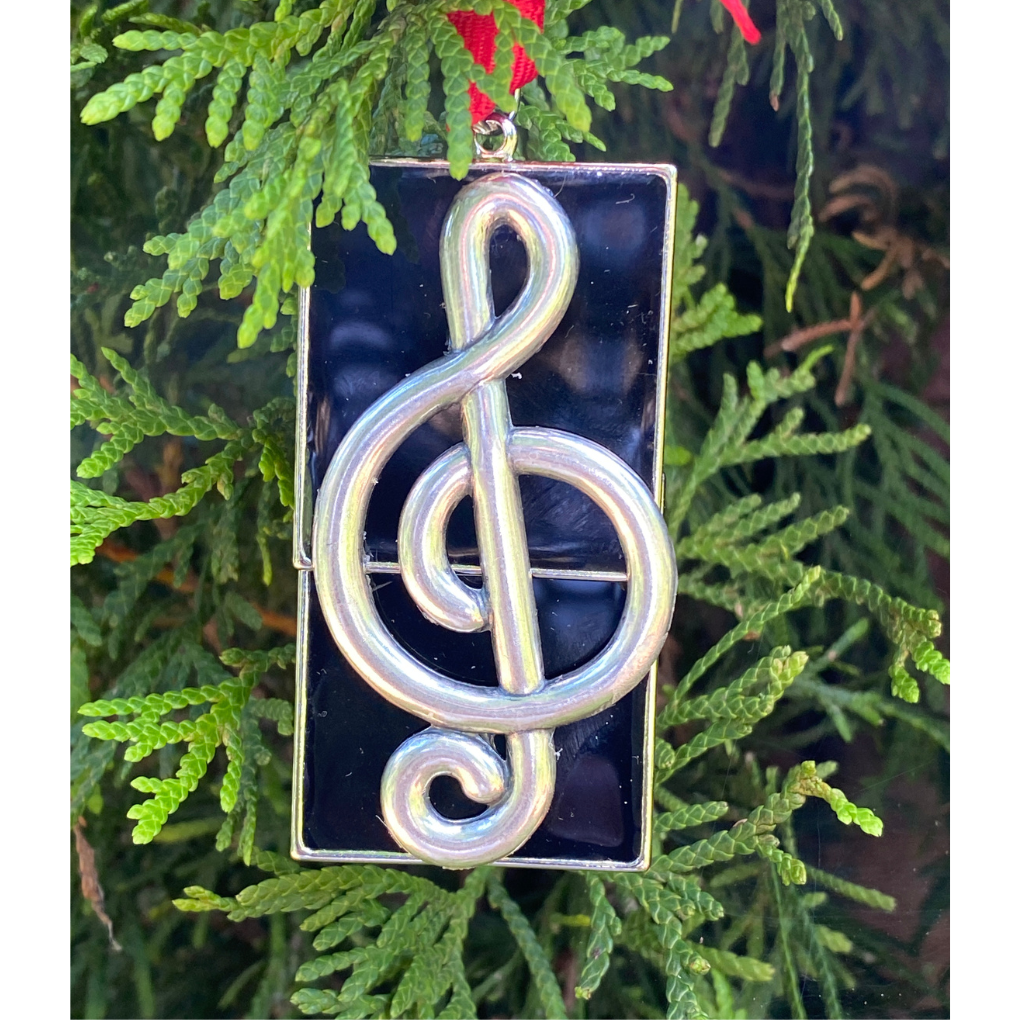 Decorative ornament with a silver treble clef symbol on a dark background, hanging on a Christmas tree.