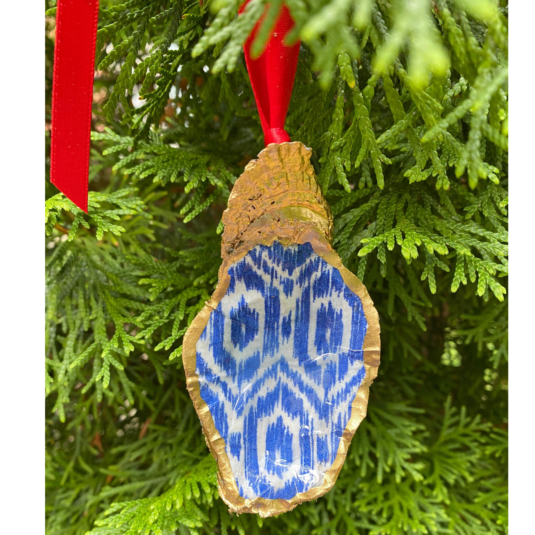 Blue Ikat Beach Christmas Ornament hung with a red ribbon