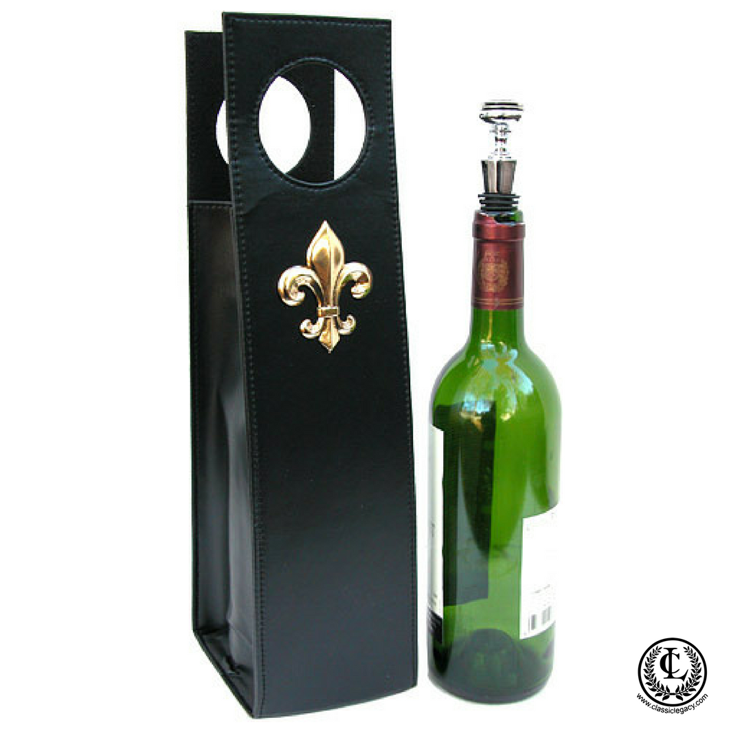 Black leather wine carrier with a gold fleur de lis emblem next to a green glass bottle with a silver stopper.