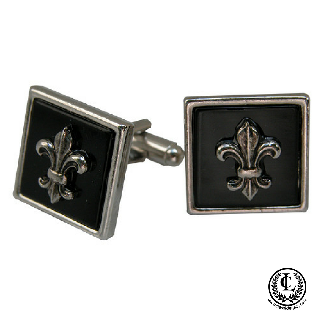 A pair of silver cuff links with a black enamel fleur-de-lis design, presented in a fabric-lined rectangular black box.