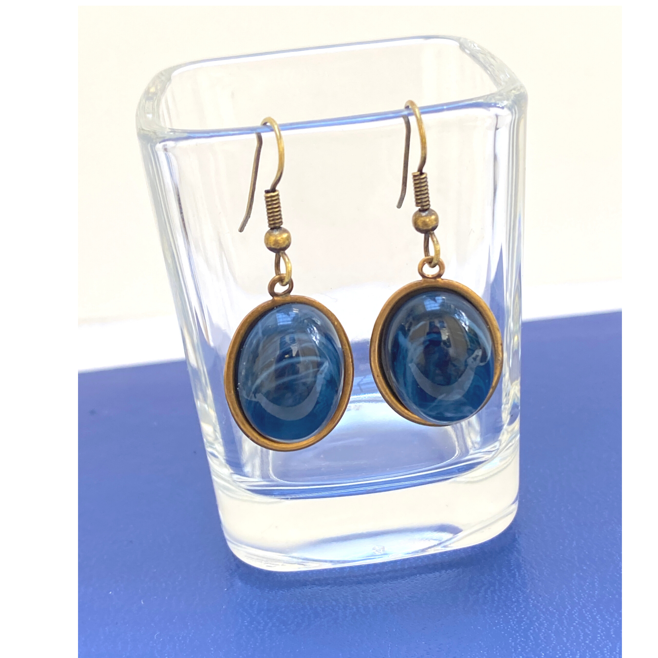 A pair of faux blue lapis earrings with antique gold setting, displayed in a clear glass vial.