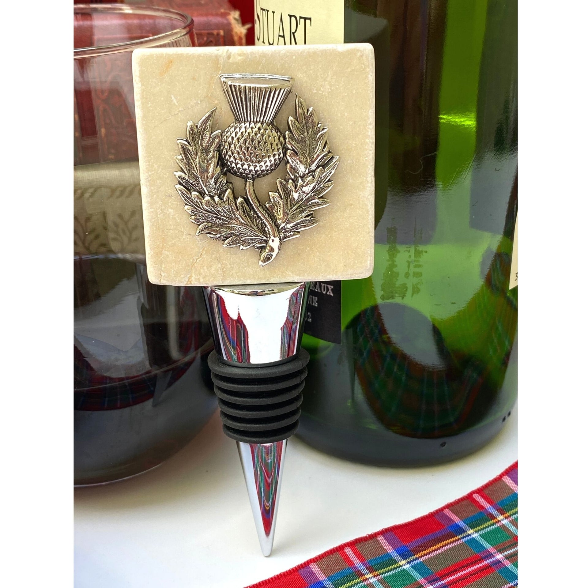 A silver thistle-designed marble bottle stopper inserted into a bottle, placed on a tartan cloth.