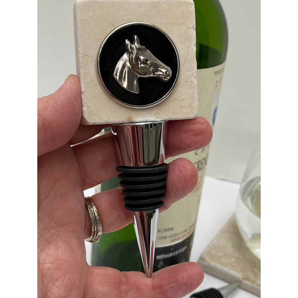 A marble bottle stopper with a silver horse head design on top, held in a person's hand, with a blurred background suggesting a wine bottle.