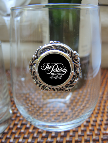 This stemless wine glass is designed to feature YOUR art, logo, or photograph.   Our stemless wine glass holds 17 ounces.  It is embellished with a silver medallion and a setting with YOUR custom logo.    This glass features the logo of The Peabody hotel.