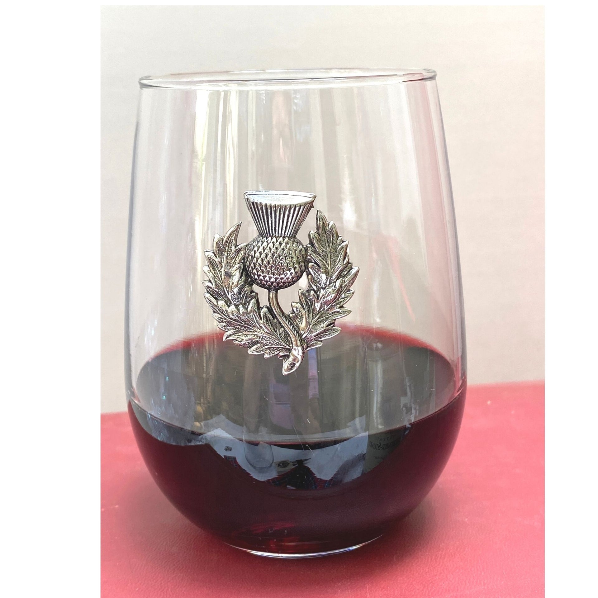 A stemless wine glass with a silver thistle design at the base, filled with red liquid, likely intended as a gift for Robert Burns Night.