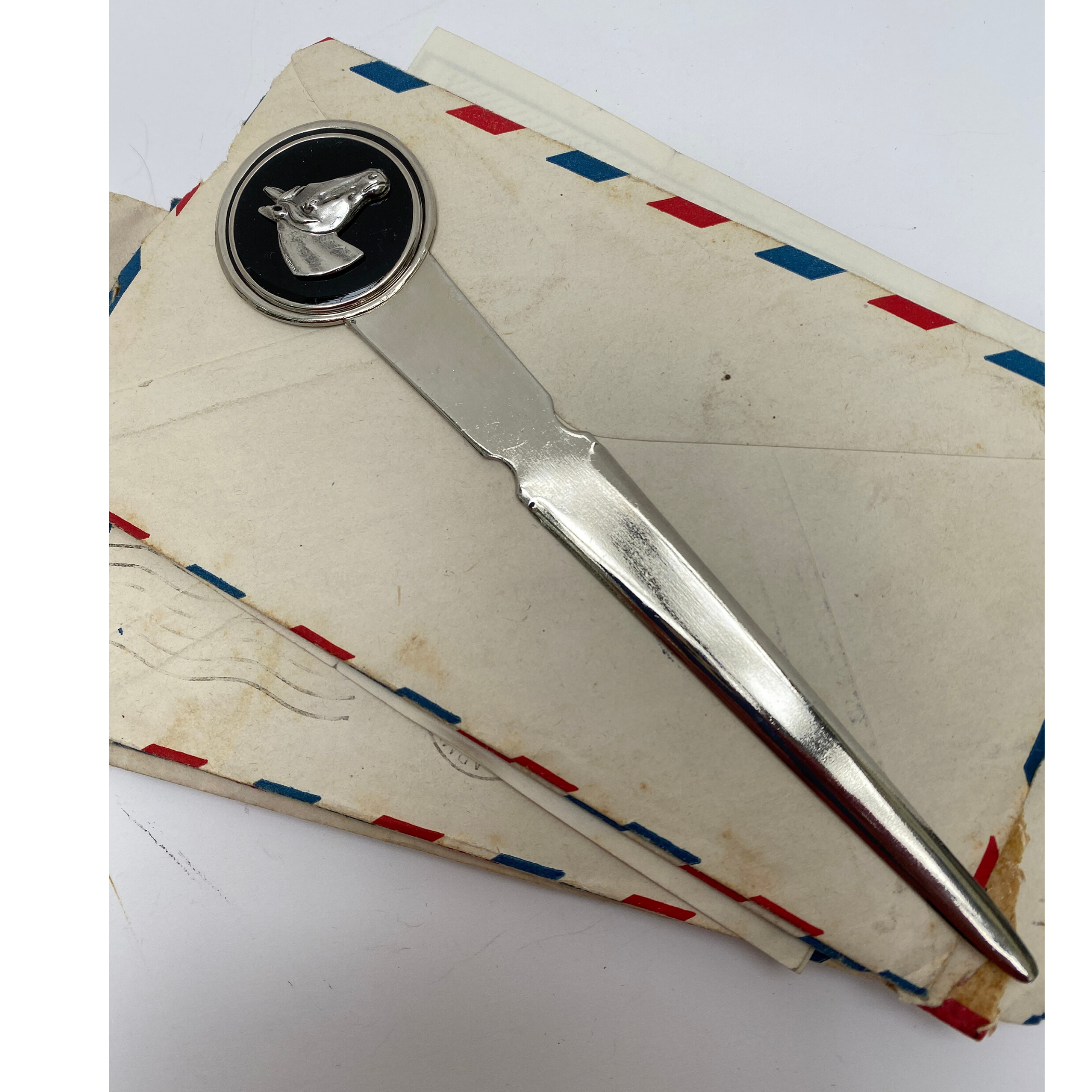 A silver letter opener with a horse head medallion design, placed on top of some envelopes.